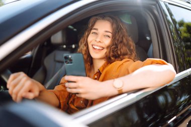Elinde telefon olan bir kadın şoför. Güzel bir kadın cep telefonuyla mesajlaşıyor ve şehir trafiğinde bekliyor. Boş zaman, seyahat, teknoloji, navigasyon.