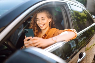 Elinde telefon olan bir kadın şoför. Güzel bir kadın cep telefonuyla mesajlaşıyor ve şehir trafiğinde bekliyor. Boş zaman, seyahat, teknoloji, navigasyon.