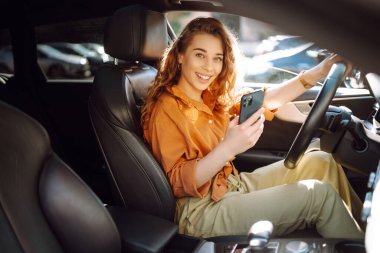 Elinde telefon olan bir kadın şoför. Güzel bir kadın cep telefonuyla mesajlaşıyor ve şehir trafiğinde bekliyor. Boş zaman, seyahat, teknoloji, navigasyon.