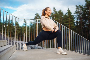 Sporcu kadın dışarıda antrenman yapıyor, esneme hareketleri yapıyor. Spor, aktif yaşam, spor eğitimi, sağlıklı yaşam tarzı..