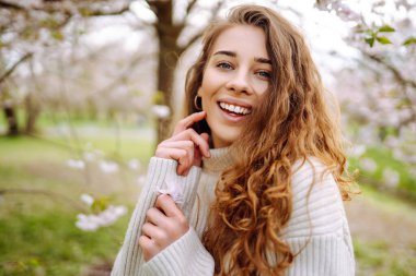 Çiçek açan bahar bahçesinde kokunun tadını çıkaran mutlu kadın. Gençlik, aşk, moda, turizm ve yaşam tarzı kavramı.