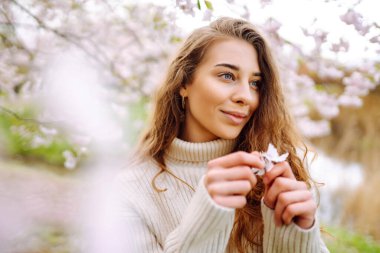 Çiçek açan bahar bahçesinde kokunun tadını çıkaran mutlu kadın. Gençlik, aşk, moda, turizm ve yaşam tarzı kavramı.