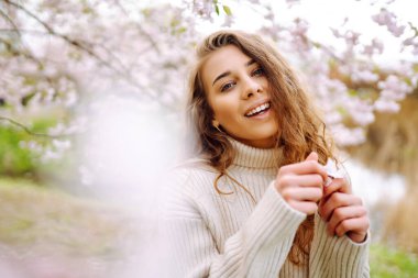 Çiçek açan bahar bahçesinde kokunun tadını çıkaran mutlu kadın. Gençlik, aşk, moda, turizm ve yaşam tarzı kavramı.