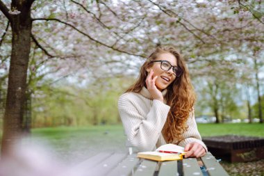 Açık havada kahve fincanı okuyan genç bir kadın. İş, blog yazma, serbest çalışma, eğitim kavramı. Dinlenme, rahatlama, rahatlama kavramı.