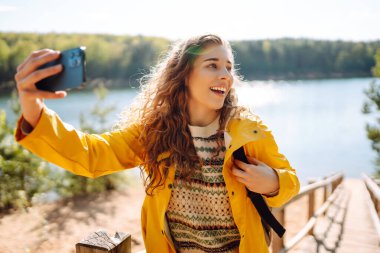 Neşeli bayan gezgin elinde akıllı telefon cihazıyla çevrede dolaşırken tatilde yeni maceranın tadını çıkaran mutlu bir kadın. Seyahat ve teknoloji