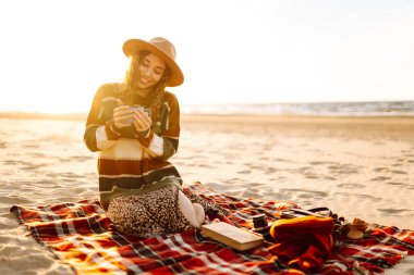 Plajda sabah kahvesi içen genç bir kadın. Seyahat, hafta sonu, rahatlama ve yaşam tarzı konsepti.