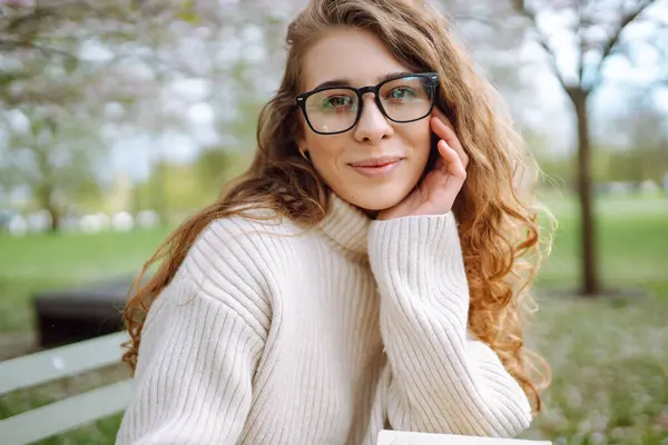 Çiçek açan bahar bahçesinde kokunun tadını çıkaran mutlu kadın. Gençlik, aşk, moda, turizm ve yaşam tarzı kavramı.