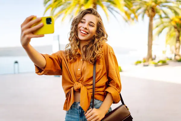 Cep telefonlu bir kadın gezgin, selfie çekiyor, seyahat blogu için Palm Tree 'nin yakınındaki bir video bağlantısıyla iletişim kuruyor. Macera, tatil konsepti.