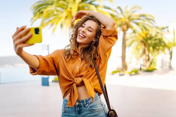 Cep telefonlu bir kadın gezgin, selfie çekiyor, seyahat blogu için Palm Tree 'nin yakınındaki bir video bağlantısıyla iletişim kuruyor. Macera, tatil konsepti.