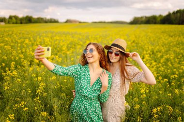 Çiçek tarlasında yürürken iki kadın selfie çeker. Moda, güzellik konsepti. Yaz manzarası.