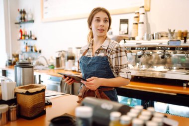 Gülümseyen kadın bardaki tezgahın önünde beklerken tabletten sipariş alıyor. Çevrimiçi sipariş. Küçük işletmeler, insanlar, paket servis ve hizmet kavramı.