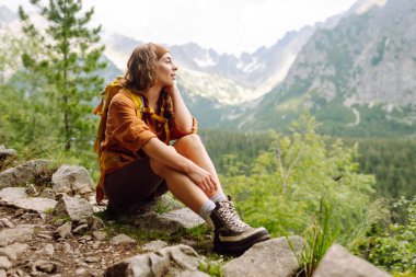 Sırt çantalı, sarı ceketli, seyahat eden dağlı bir kadın. Temiz hava. Turizm, seyahat, yürüyüş kavramı.