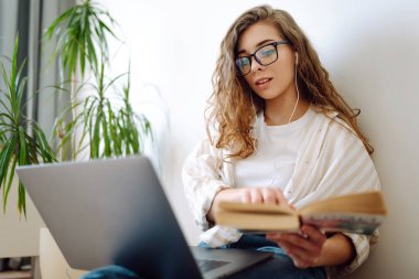 Genç bir kadın evde oturuyor, dizüstü bilgisayar kullanıyor, kulaklıkla müzik dinliyor. Serbest, çevrimiçi kurs. İnternetten alışveriş. 