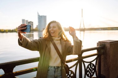 Cep telefonu olan mutlu bir kadın, selfie çekiyor, arkadaşlarıyla iletişim kuruyor, dışarıda blog yazıyor. Yaşam tarzı, seyahat, turizm, doğa, aktif yaşam.