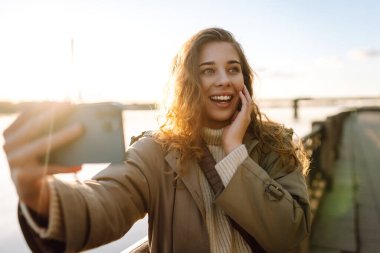 Cep telefonu olan mutlu bir kadın, selfie çekiyor, arkadaşlarıyla iletişim kuruyor, dışarıda blog yazıyor. Yaşam tarzı, seyahat, turizm, doğa, aktif yaşam.