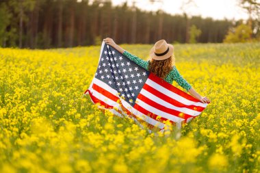 Amerikan bayrağıyla genç bir kadının portresi, sahada günbatımının keyfini çıkarıyor. 4 Temmuz. Bağımsızlık Günü. Vatansever bayram.