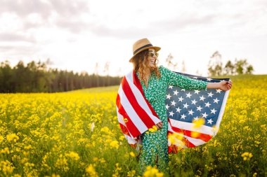 Amerikan bayrağıyla genç bir kadının portresi, sahada günbatımının keyfini çıkarıyor. 4 Temmuz. Bağımsızlık Günü. Vatansever bayram.