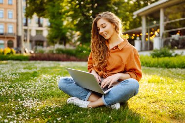 Yeşil çimlerde dizüstü bilgisayarı olan güzel bir kadın. Eğitim çevrimiçi. IT, uzaktan kumanda. İş, blog yazma, serbest çalışma kavramı.
