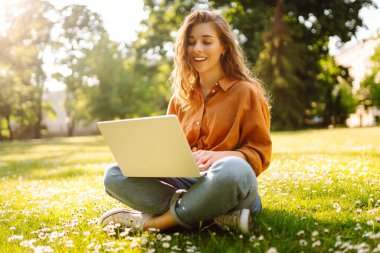 Yeşil çimlerde dizüstü bilgisayarı olan güzel bir kadın. Eğitim çevrimiçi. IT, uzaktan kumanda. İş, blog yazma, serbest çalışma kavramı.