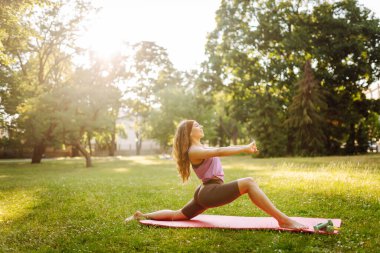 Park 'ta yoga yapan genç bir kadının portresi. Spor, aktif yaşam, sağlıklı yaşam tarzı.