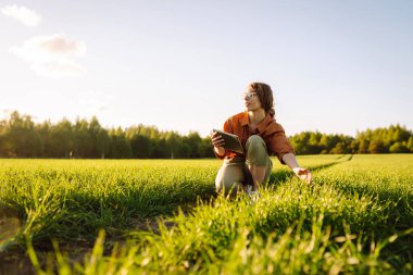 Modern tabletli bir kadın çiftçi filizleri eliyle değerlendirir, tarladaki yeşil filizleri. Tarım, bahçıvanlık veya ekoloji kavramı.