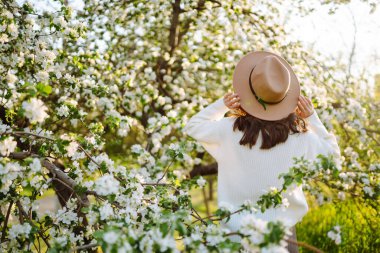 Genç bir kadın bir bahar parkında çiçek açan bir ağacın yanında duruyor. Gençlik, aşk, moda, turizm ve yaşam tarzı kavramı.