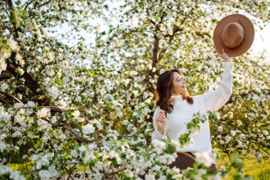 Genç bir kadın bir bahar parkında çiçek açan bir ağacın yanında duruyor. Gençlik, aşk, moda, turizm ve yaşam tarzı kavramı.