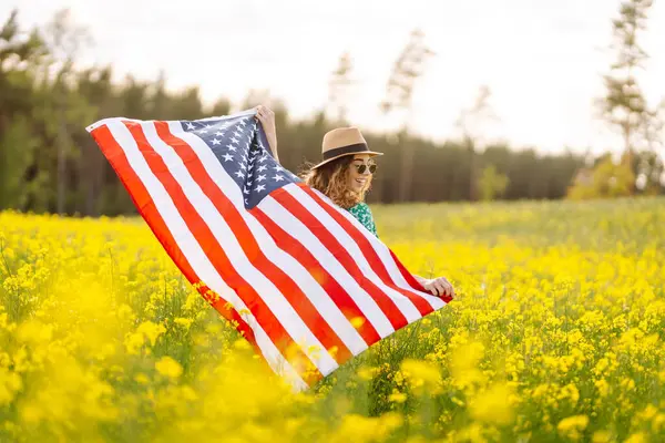 Amerikan bayrağıyla genç bir kadının portresi, sahada günbatımının keyfini çıkarıyor. 4 Temmuz. Bağımsızlık Günü. Vatansever bayram.