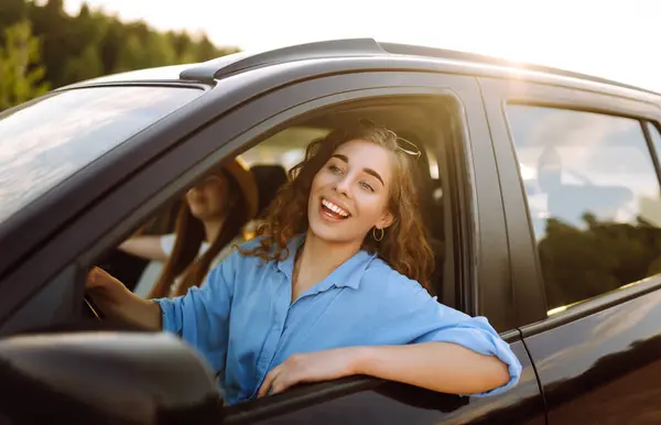 Two trendy attractive young woman singing along to the music as they drive along in the car through town. Beautiful female friends in the car enjoy a car trip together.