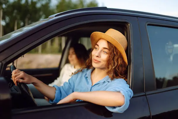 Two trendy attractive young woman singing along to the music as they drive along in the car through town. Beautiful female friends in the car enjoy a car trip together.