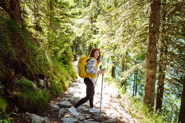 Young woman with backpacks and walking sticks hiking in nature. Adventure, travel, sport, active life.