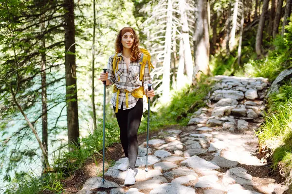 Young woman with backpacks and walking sticks hiking in nature. Adventure, travel, sport, active life.
