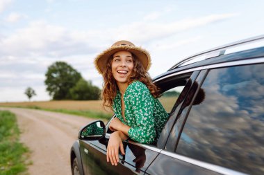 Genç bir kadın araba yolculuğunun tadını çıkarıyor. Yaz tatili, tatiller, seyahat, yol gezisi ve insan konsepti - doğadaki genç kadın..