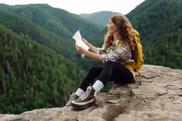 Beautiful woman traveler holds a map, explores hiking trails in the mountains. The concept of travel, vacation, adventure.
