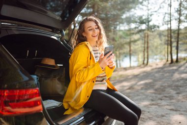 Bagajda telefonuyla oturan genç bir kadın. Yaşam tarzı, seyahat, turizm, doğa, aktif yaşam.