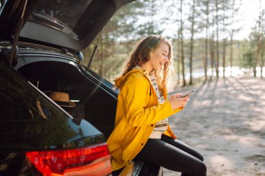 Bagajda telefonuyla oturan genç bir kadın. Yaşam tarzı, seyahat, turizm, doğa, aktif yaşam.