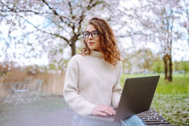 Parkta oturup dizüstü bilgisayar kullanan güzel bir kadın. Bağımsızlık, teknoloji, eğitim, iş dünyası, blog konsepti.