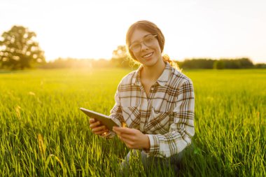 Yeşil tarlada modern tableti olan bir kadın çiftçi. Çiftlik gelişimi ve bahçıvanlık kavramı.