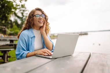 Dışarıda çalışan genç bir kadın güzel havanın tadını çıkarıyor. Bağımsızlık, teknoloji, eğitim, iş dünyası, blog konsepti.