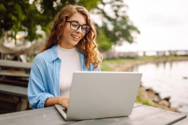 Dışarıda çalışan genç bir kadın güzel havanın tadını çıkarıyor. Bağımsızlık, teknoloji, eğitim, iş dünyası, blog konsepti.