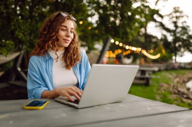 Dışarıda çalışan genç bir kadın güzel havanın tadını çıkarıyor. Bağımsızlık, teknoloji, eğitim, iş dünyası, blog konsepti.