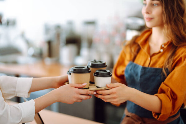 Female barista giving order to client, coffee in cardboard cups. Takeaway food concept.