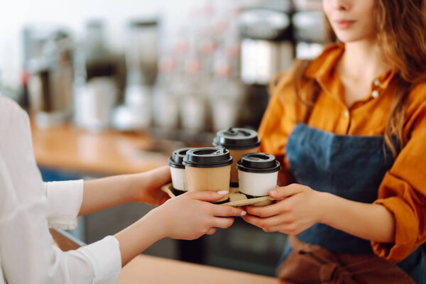 Female barista giving order to client, coffee in cardboard cups. Takeaway food concept.