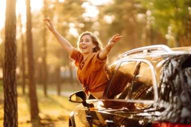 Genç kadın arabada dinleniyor ve gün batımının tadını çıkarıyor. Yaşam tarzı, seyahat, turizm, doğa, aktif yaşam.