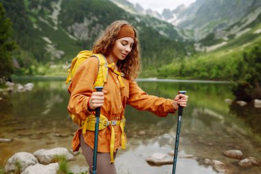 Sarı bir sırt çantasıyla aktif bir kadın ormanların ve kayalıkların arasında dağlarda yürüyüş parkurları boyunca seyahat ediyor. Yürüyüş kavramı, aktif yaşam tarzı. Maceralar.