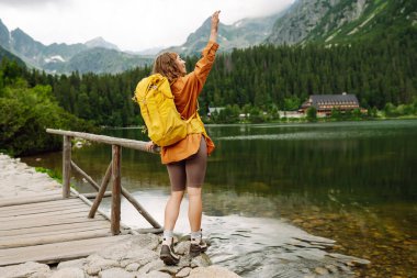 Sarı bir sırt çantasıyla aktif bir kadın ormanların ve kayalıkların arasında dağlarda yürüyüş parkurları boyunca seyahat ediyor. Yürüyüş kavramı, aktif yaşam tarzı. Maceralar.