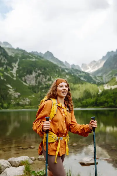 Active woman with a yellow hiking backpack traveling along hiking trails in the mountains among forests and cliffs. Concept of trekking, active lifestyle. Adventures.
