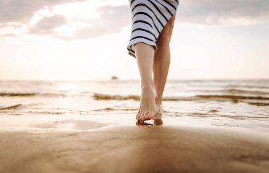 Yakın plan, genç bir kadının yaz plajında deniz suyu ve kum dalgası boyunca yürümesi. Seyahat, hafta sonu, rahatlama ve yaşam tarzı konsepti.