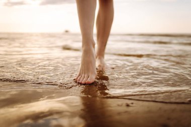 Yakın plan, genç bir kadının yaz plajında deniz suyu ve kum dalgası boyunca yürümesi. Seyahat, hafta sonu, rahatlama ve yaşam tarzı konsepti.