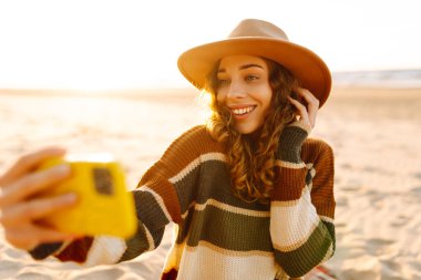 Selfie zamanı. Gün batımında deniz kenarında poz veren genç bir kadın. Seyahat, yaşam tarzı, moda, blog yazma.